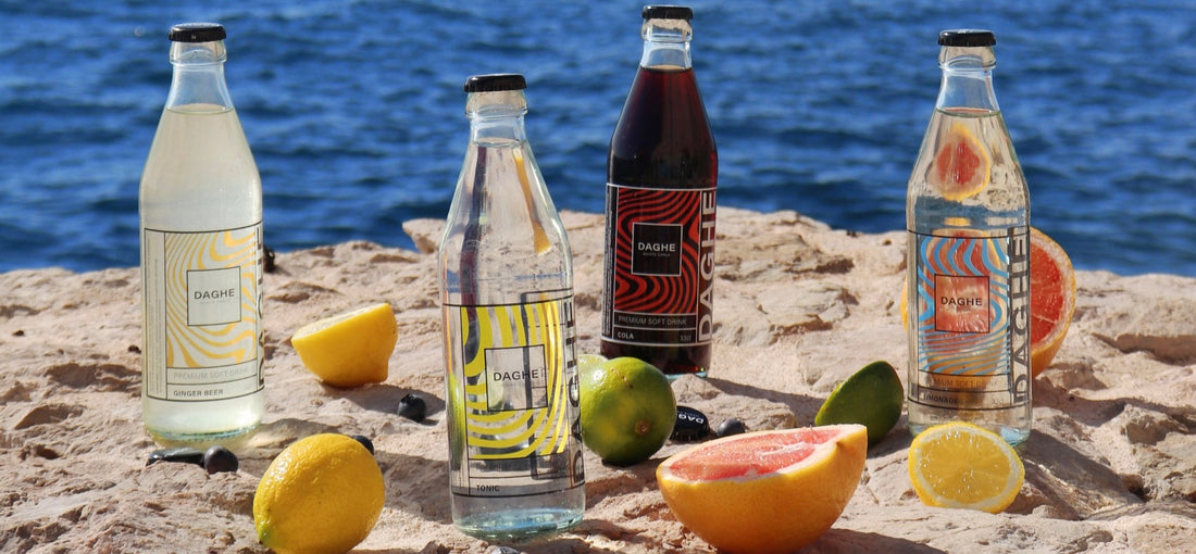 Les quatre saveurs Daghe Monte Carlo : Ginger beer, Tonic, Cola et Limonade. Elles sont posées sur un rocher en bord de mer, entourées de pamplemousse, citrons et myrtilles.